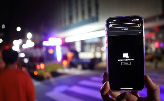 A Kakao user holds up a phone showing an error page as firefighters arrive on the scene of a fire that broke out at SK C&C in Pangyo, Gyeonggi, on Saturday. [NEWS1]