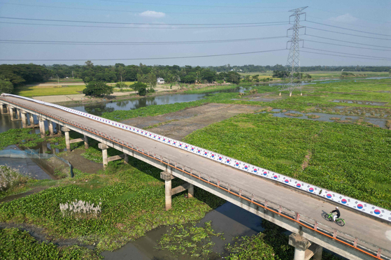 In this aerial photograph taken on Nov. 16, a rickshaw makes its way across a bridge decorated with a 3.5-kilometer (2.2-mile) Korean flag put up by Bangladeshi chemist Abu Kowsir from his home to a neighboring village in Bancharampur, Bangladesh.  [AFP/YONHAP] 