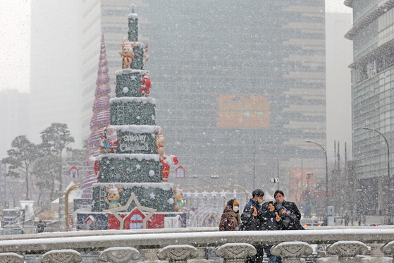  People take a selfie with a giant Christmas tree at the background at Cheonggye Plaza in downtown Seoul during heavy snowfall on Thursday. [NEWS1] 