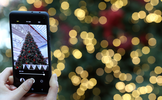 A visitor to the Hyundai Seoul in Yeouido, western Seoul, takes a photo of a Christmas tree set up at the department store on Dec. 11. [YONHAP] 