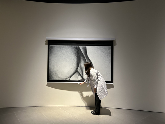 A staff at the Martin Margiela exhibition lowers the projector screen of ″Body Part b&w″ (2018-20) as part of the piece's performance. [SHIN MIN-HEE]