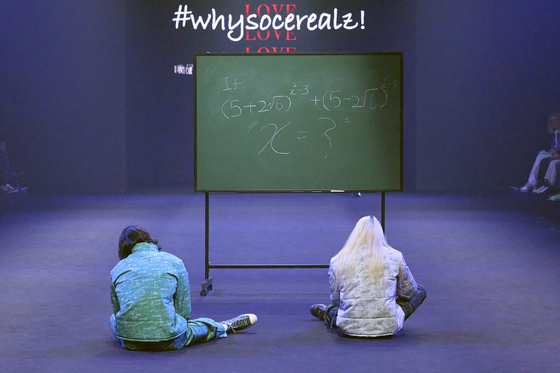 A scene from #whysocerealz!'s Seoul Fashion Week 2023 Fall/Winter show last month. Here shows two models sitting in front of a chalkboard that is covered with equations, appearing stumped. [#WHYSOCEREALZ!]