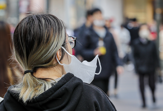 A pedestrian walks half-masked in the streets of Myeong-dong in Jung District, central Seoul, on March 29. [NEWS1]