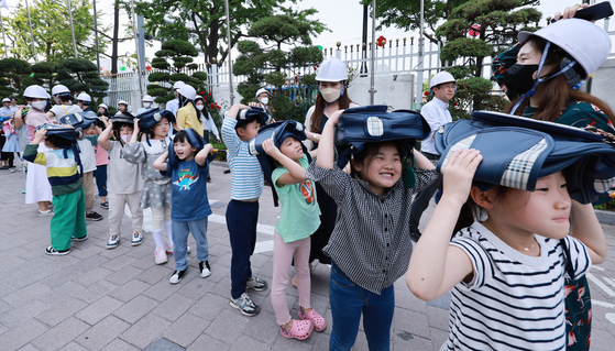 Children hold their school bags over their heads as they take part in a civil evacuation drill at the Central Government Complex in Jongno District, central Seoul, on May 16. [YONHAP]