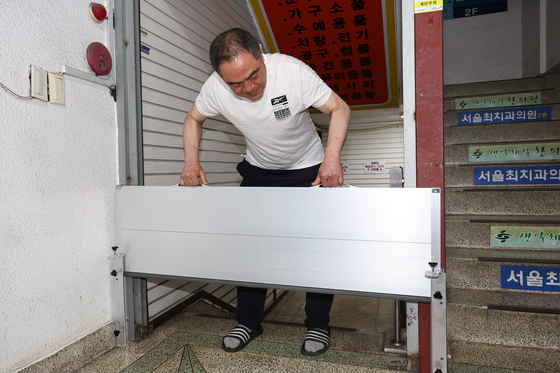 A shop owner at a traditional market in Seoul on Sunday places a steel panel that would prevent waters from getting into the basement during heavy rain. [YONHAP]
