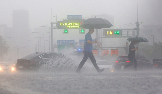 People cross a sidewalk in Yeouido, western Seoul, on Thursday as heavy rain falls in the area. [YONHAP] 
