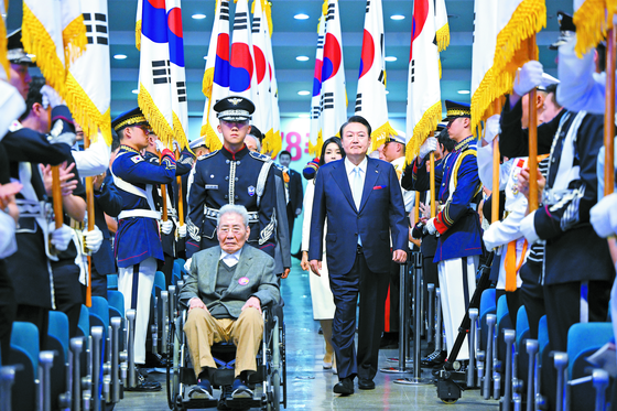 President Yoon Suk Yeol, right, enters with 100-year-old independence fighter Oh Seong-gyu, pushed in a wheelchair by a military officer, for the 78th Liberation Day ceremony at a Ewha Womans University auditorium in Seodaemun District, central Seoul on Tuesday. [PRESIDENTIAL OFFICE] 