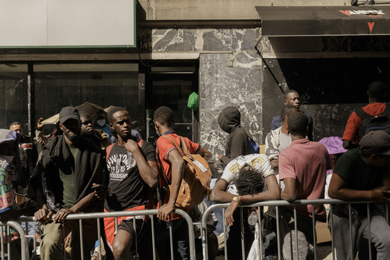 Migrants waiting to be processed queue outside of the Roosevelt Hotel in Manhattan, on Tuesday, Aug. 1, 2023. Gov. Kathy Hochul said the state was weighing whether it would challenge federal law and issue work permits directly to recent asylum seeker. [Jeenah Moon/The New York Times]