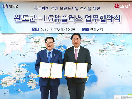 LG UPlus's head of electric vehicle business Hyun Joon-yong, right, and Wando governor Shin Woo-cheol sign a memorandum of understanding in Wando, South Jeolla, on Tuesday. [LG UPLUS]