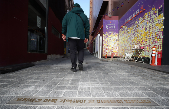 A person on Friday walks up the alleyway where the Halloween crowd crush occurred on the night of Oct. 29 last year. A sign on the ground reads, "We still have names to remember." [NEWS1]