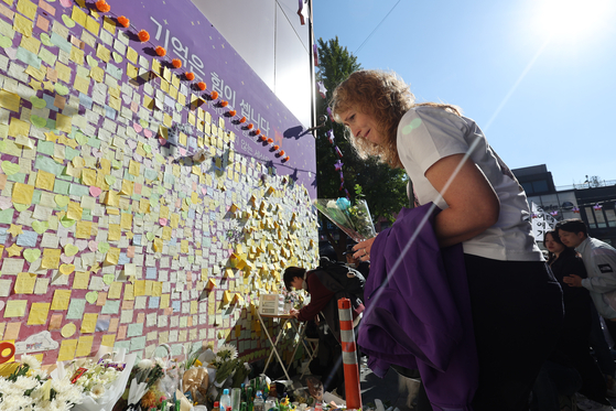 A family member of one of the foreign victims killed in the Itaewon crowd crush a year ago visits the narrow alleyway where the tragedy occurred, along with others who lost loved ones. Some 26 foreigners from 14 countries were among the 159 disaster victims. [YONHAP]