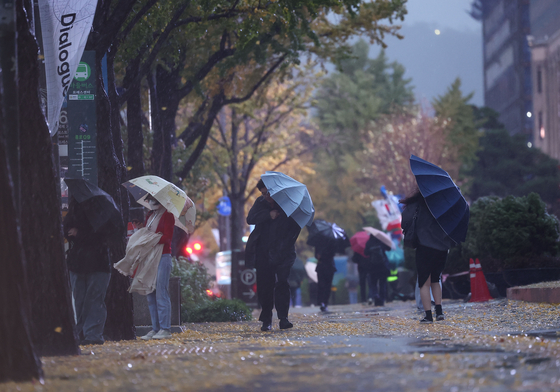 Seoulites passing through Sejongno in downtown Seoul on Monday try to shield themselves from the strong wind and rain. [YONHAP]