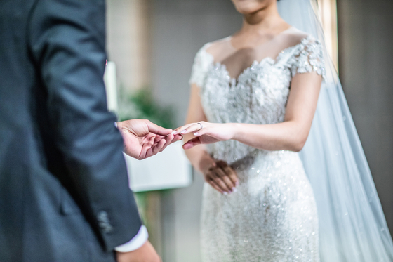 A groom puts a ring on a bride's finger. [SHUTTERSTOCK]