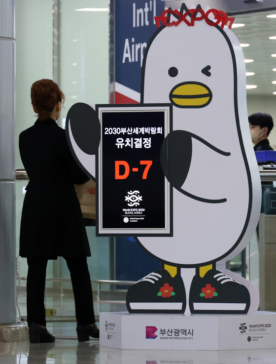 Busan's feathered mascot Boogi holds up a sign indicating that there are seven days left until the vote for the hosting city of the World Expo 2030, at Gimhae International Airport in South Gyeongsang on Tuesday. Korean politicians and businessmen alike are making final efforts in support of Busan's bid for the expo ahead of the final vote scheduled for Tuesday in Paris. [YONHAP]
