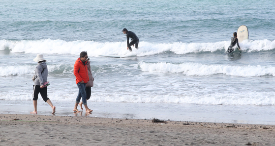 People walk along the coast in bare feet at Iho Tewoo Beach, Jeju, on Sunday. [NEWS1]