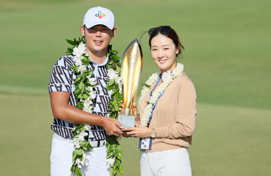Kim Si-woo, left, poses with his wife Oh Ji-hyun and the trophy after putting in to win on the 18th green during the final round of the Sony Open in Hawaii at Waialae Country Club on Jan. 15, 2023 in Honolulu, Hawaii. [AFP/YONHAP]