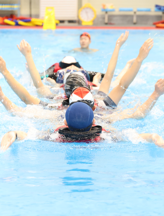 Elementary school teachers participate in a survival swim lesson at the Korea Coast Guard’s training pool in Busan on Thursday. The lesson was arranged by the Busan Metropolitan City Office of Education and the Coast Guard to improve the ability of teachers to teach swimming. [YONHAP]