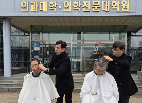 Medical professors at Kangwon National University shave their heads in front of the school on Tuesday to protest the university's request to increase its enrollment quota from 49 to 140. [KANGWON NATIONAL UNIVERSITY] 