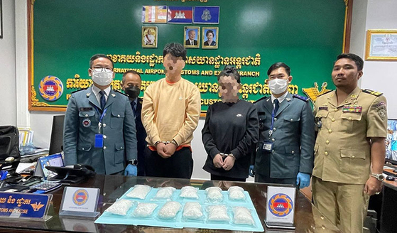 Two handcuffed Korean nationals take a photo with Cambodian border control and customs officials after the crackdown at Phnom Penh International Airport. [KHMER TIMES]