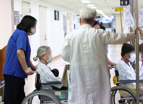 A doctor wearing a white gown helps his patients ride an elevator at a general hospital in Seoul on Friday morning. [YONHAP] 