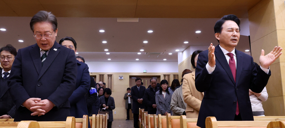 Democratic Party Chairman Lee Jae-myung, left, and former Land Minister Won Hee-ryong of the People Power Party, both running for Incheon’s Gyeyang-B District in the upcoming April 10 general election, attend an Easter service at a church in Gyeyang District, Incheon, Sunday morning. [JOINT PRESS CORPS]