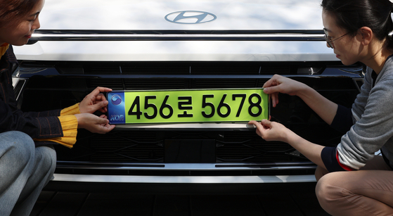 Two public officials hold up a light green license plate to be affixed to a corporate cars with a price tag exceeding 80 million won last November in Sejong. [YONHAP]  