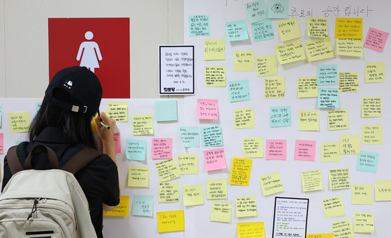 A woman writes a letter of condolence to a subway worker outside a public restroom at Sindang Station in Jung District, central Seoul, on Sep. 16, 2022, two days after the worker was stabbed to death by Jeon Joo-hwan, her former colleague. [YONHAP]