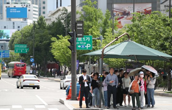 With the Seoul daytime temperature reaching 30 degrees Celcius, people gather under the sun shelter located at four-way crosswalk in Jong District, Soul on Monday afternoon. [NEWS1]