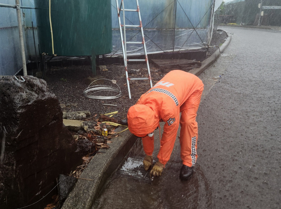 A fire official unclogs sewage on Sehwa-ri Street in Seogwipo, Jeju, which had been flodded due to monsoon rains on Thursday. [JEJU FIRE DEPARTMENT] 