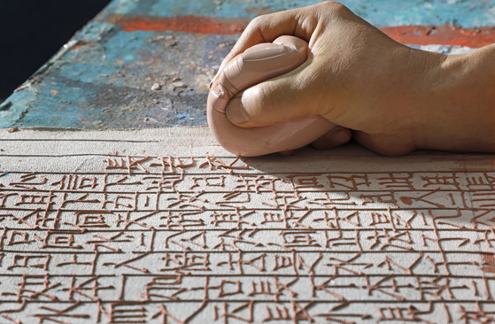 Artist Shin Yong-il meticulously writes Chinese letters with a mixture of soil and water. The letters are from “Jikji Simche Yojeol,” which roughly translates to "Anthology of Great Buddhist Priests’ Zen Teachings" at his studio in Gunpo, Gyeonggi. [PARK SANG-MOON] 