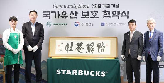 From second from left, Starbucks Korea CEO Sohn Jeong-hyun, KHS Administrator Choi Eung-chon and National Trust for Cultural Heritage Chairman Kim Jong-kyu pose for the camera during Thursday’s Starbucks Hwangudan store's reopening ceremony held in Jung District, central Seoul. Pictured in the middle is a calligraphic work by independence fighter Oh Se-Chang. [STARBUCKS KOREA]