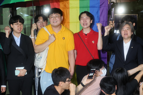 So Seong-wook, second left, and Kim Yong-min, second right, who filed a lawsuit against the National Health Insurance Service demanding equal spousal coverage to a same-sex couple in 2021 chant slogans in front of the Supreme Court in Seocho District, southern Seoul, on Thursday. [YONHAP]