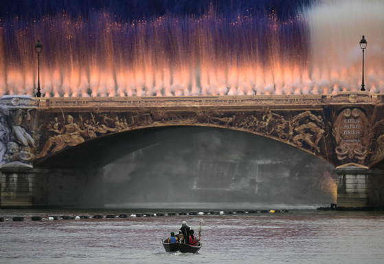 The Olympic torch is carried on a boat under the Austerlitz bridge at the start of the opening ceremony for the Paris Olympics.  [AFP/YONHAP]