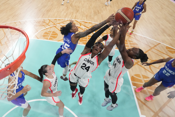 Gabby Williams of France goes up for a rebound with Aaliyah Edwards, center, and Kayla Alexander, of Canada, during a women's basketball game at the Paris Olympics on Monday in Villeneuve-d'Ascq, France. [AP/YONHAP]