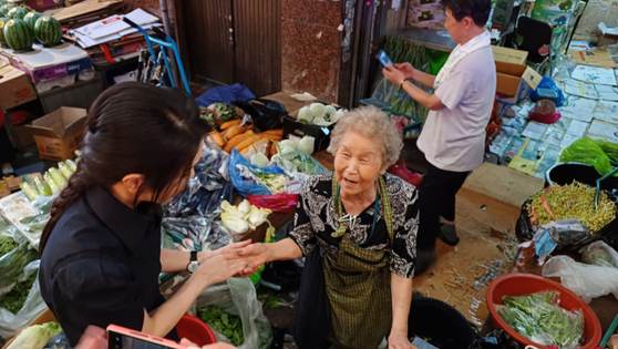 First lady Kim Keon Hee, left, is seen talking to a vendor at a traditional market in Bupyeong District, Busan, while shopping for groceries on Tuesday. [SCREEN CAPTURE]