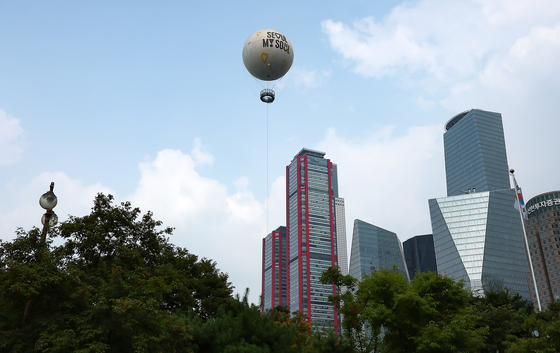 A moon-shaped tethered balloon, dubbed “Seouldal,” is seen in front of high-rise buildings while it floats above Yeouido Park in western Seoul on Sunday afternoon. [NEWS1]