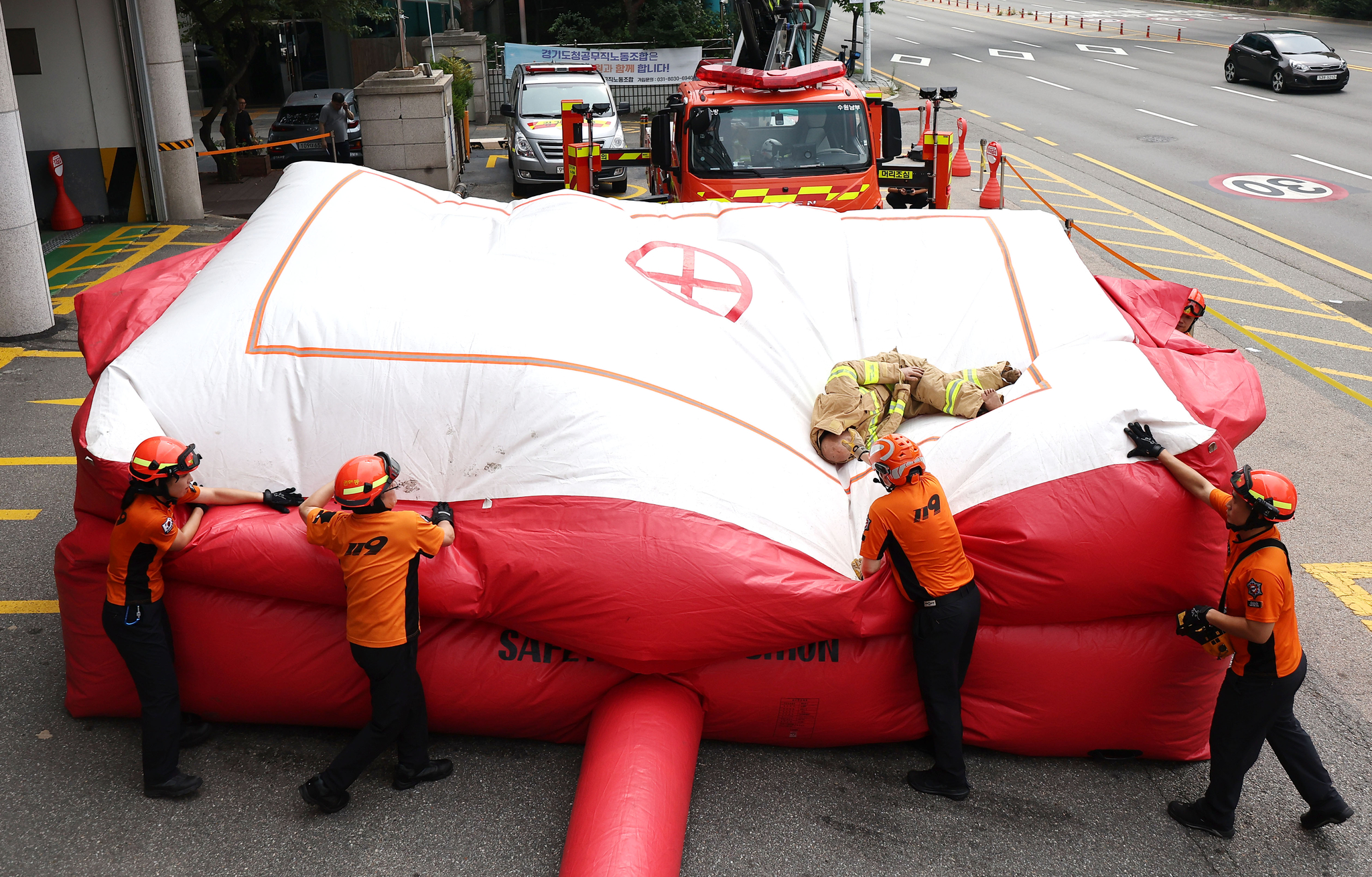 Fire authorities conduct a drill involving landing on an inflatable fire rescue mattress at the Gyeonggi Fire and Disaster Headquarters in Gwonseon District, Gyeonggi, on Monday. Concerns rose over the safety of firefighters' rescue mattresses after it was revealed that two of the seven victims in Thursday's Bucheon hotel fire died after jumping onto one while trying to escape. [JOINT PRESS CORPS]