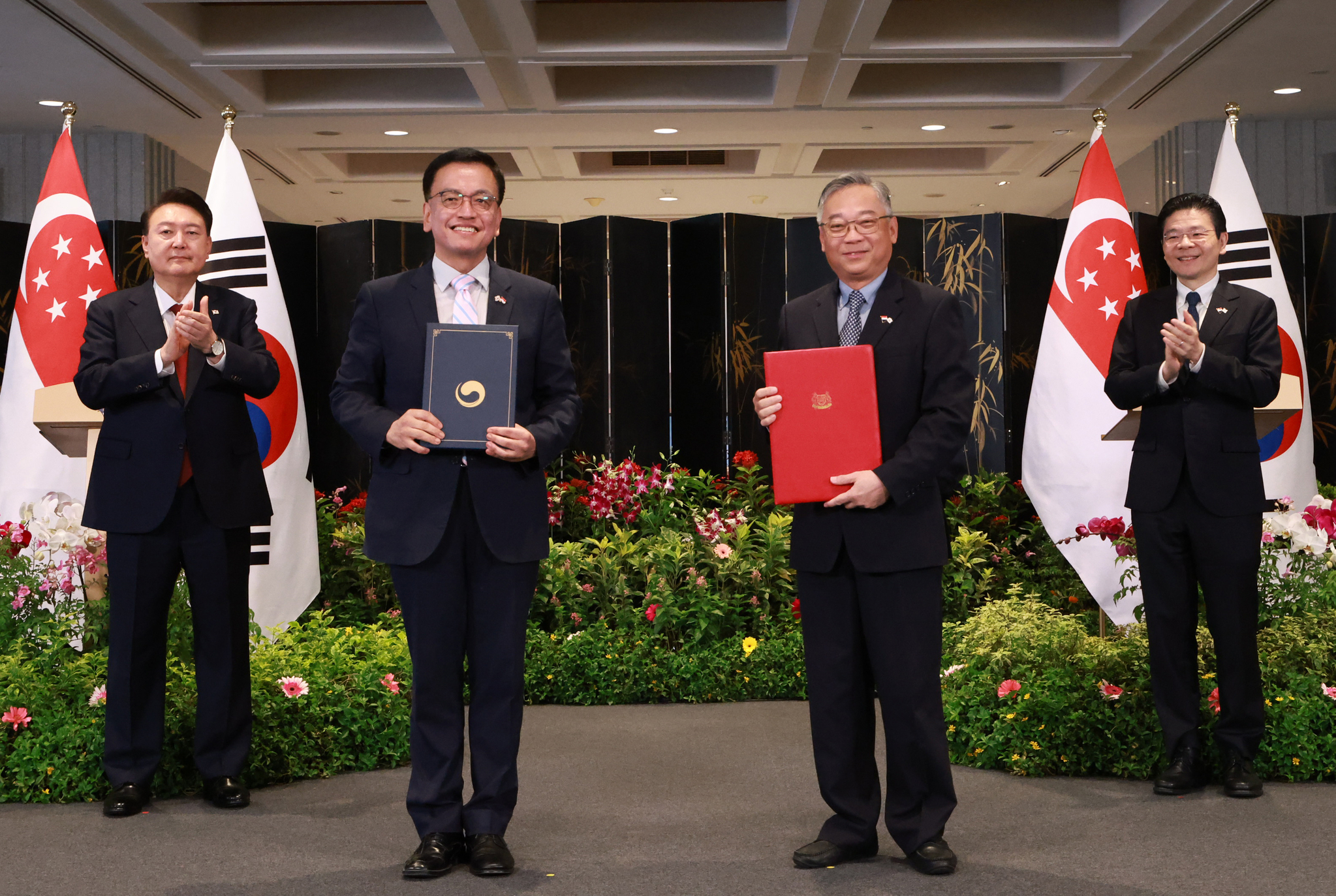 Korean President Yoon Suk Yeol, left, and Singaporean Prime Minister Lawrence Wong, right, watch Finance Minister Choi Sang-mok, center left, and his Singaporean counterpart, Gan Kim Yong, center right, sign a memorandum of understanding on liquefied natural gas cooperation at the Parliament House in Singapore on Wednesday. [JOINT PRESS CORPS]