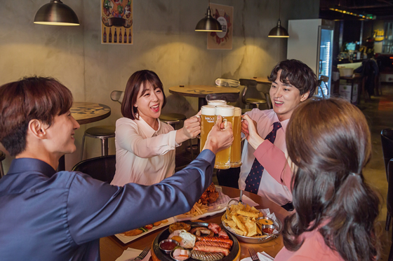 Relatively younger workers enjoy beer and food at a restaurant with smiles on their faces. [GETTY IMAGES BANK]