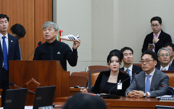 Kim Jung-joong, head of the Adidas Korea store owners' committee, speaks while holding an Adidas shoe at a parliamentary audit hearing held at the National Assembly building on Monday. Adidas Korea general manager Peter Kwak, far right, also attended to give a testimony on the Korean branch's alleged unfair practices toward its franchise stores. [YONHAP]