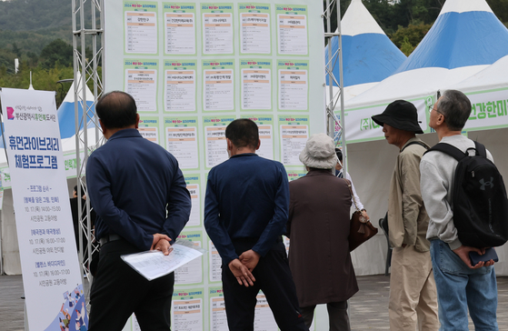Older job seekers look through a recruiting board at a job fair in Busan in October. [SONG BONG-KEUN