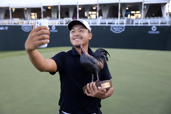 Kevin Yu poses with the trophy on the 18th green as he takes a selfie after his winning putt during the first playoff hole of the final round of the Sanderson Farms Championship 2024 at the Country Club of Jackson on Oct. 06 in Jackson, Mississippi. [GETTY IMAGES]