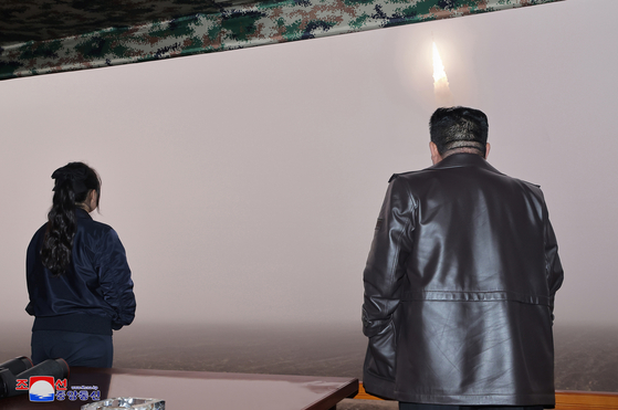North Korea fires the new Hwasong-19 intercontinental ballistic missile, guided by its leader, Kim Jong-un, in this photo released by North Korea's state-run Korean Central News Agency on Friday. Kim's daughter Ju-ae, left, also attended the missile launch. [SCREEN CAPTURE]