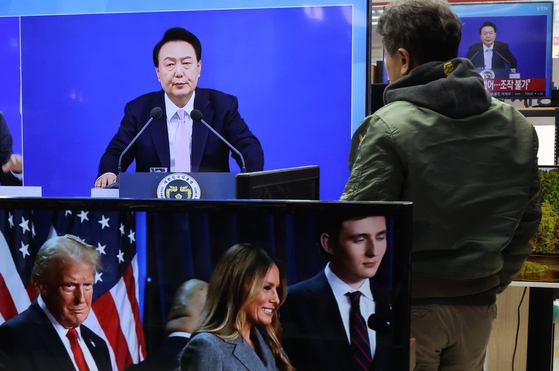 A passerby watches a broadcast about South Korean President Yoon Suk Yeol's national address at an electronics store in Yongsan District, central Seoul, on Thursday. On the television in front, a report about U.S. President-elect Donald Trump is being broadcast. [YONHAP]
