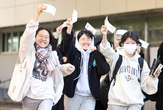 Students taking the College Scholastic Ability Test smile while holding their exam identification slips at a high school in Daegu on Wednesday, the day before the exam. [YONHAP] 
