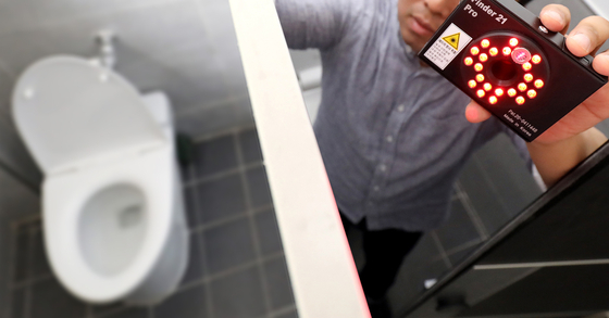 A man looks for hidden cameras in a bathroom stall with a detection device in 2021. The photo is not related to the article. [YONHAP]