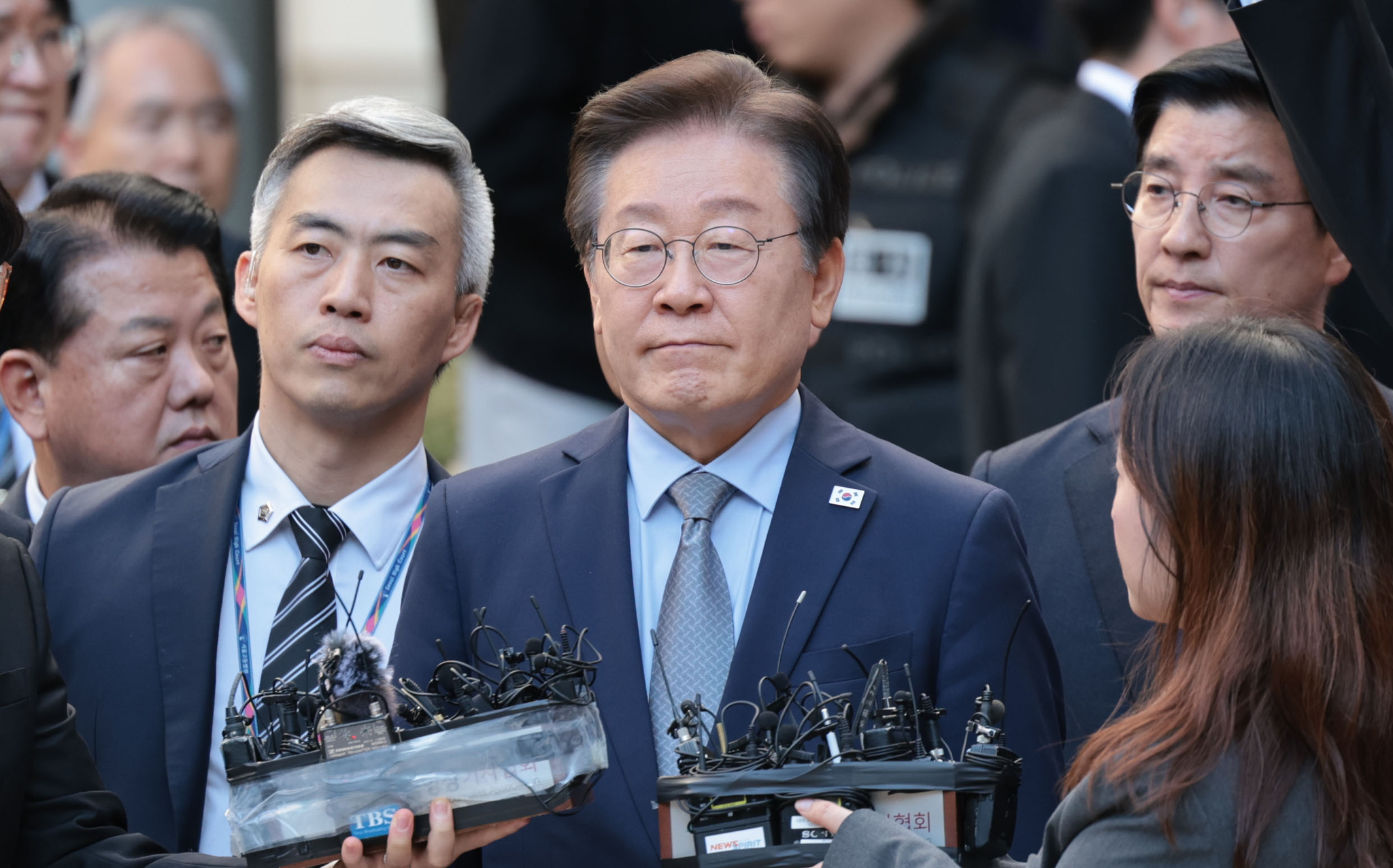 Democratic party leader Lee Jae-myung, center, answers reporters' questions outside the Seoul Central District Court in southern Seoul on Nov. 15, after the court sentenced him to a suspended one-year prison term for lying during the 2022 presidential election campaign. [YONHAP]