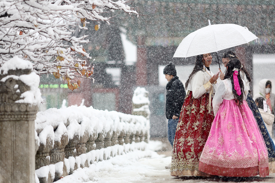 People wearing hanbok (traditional Korean dress) chat as they view the snow-covered Gyeongbok Palace in central Seoul on Wednesday. [YONHAP]  