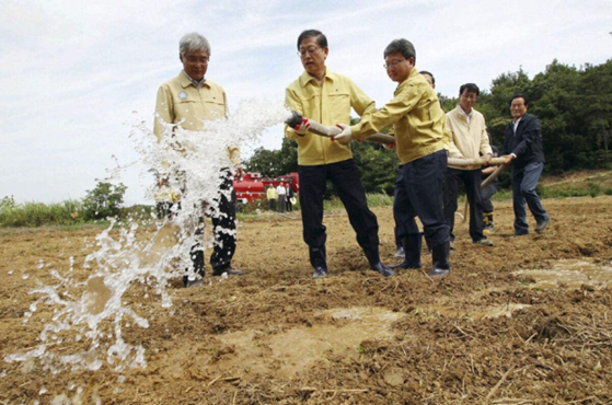 A farmer sprays water on a dry rice paddy while inspecting farmland hit by months of drought in Hwaseong, Gyeonggi, on June 26. [AP]