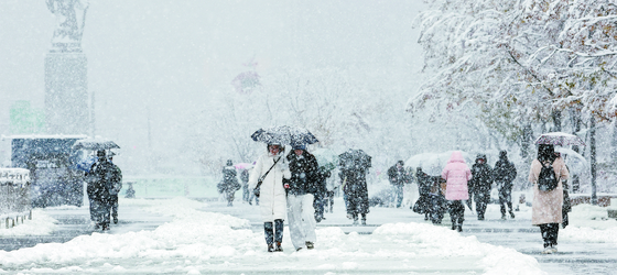 People navigate snow-covered roads in Jongno District, central Seoul, on Thursday morning. [YONHAP]
